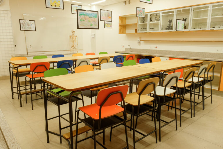 sala de aula com quatro mesas coletivas altas e com banquetas laminadas de cores diversas