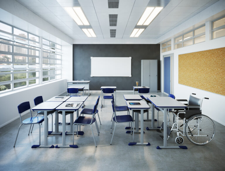 Uma sala de aula com conjuntos de mesas e cadeiras onde um dos conjuntos possui uma mesa para cadeira de rodas